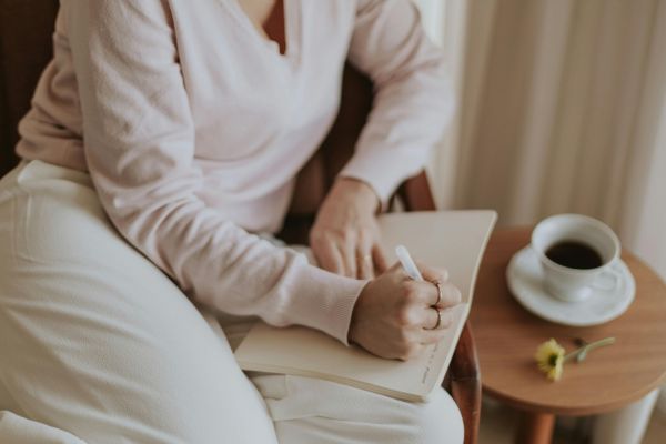 Woman sitting with morning coffee and journal, mapping resolutions for the new year.
