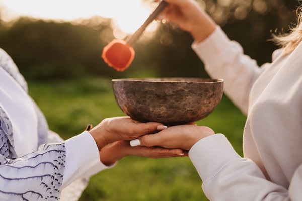 Close up of the hands of two women enjoying a sound bowl therapy technique together in the garden.