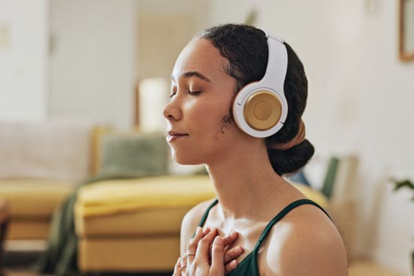 Woman doing meditation and yoga in headphones while listening to calm music, at peace in a living room.