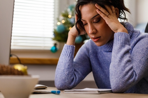 Portrait of stressed out young woman sitting at her desk at the office, head in hands, worried while working during Christmas holidays.