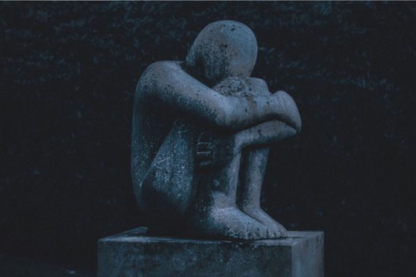 Statue of a person sat holding their arms around their knees.