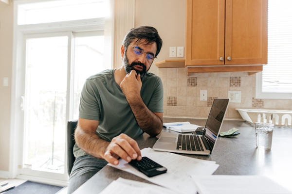Man using a calculator and laptop to pay bills