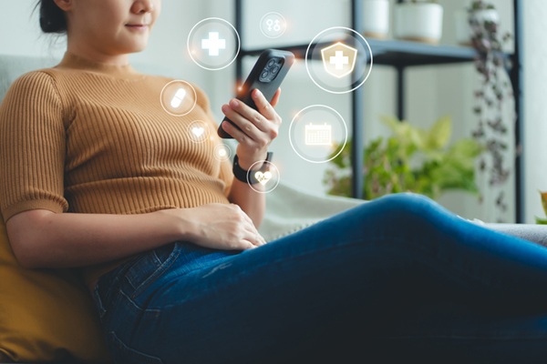 Woman sitting on the couch utilizing telemedicine with AI on her phone.
