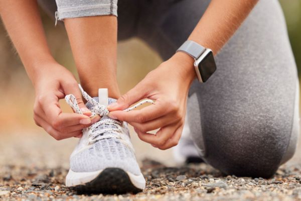 A person tying their running shoe wearing a step tracker. Preparing for a walk or run.