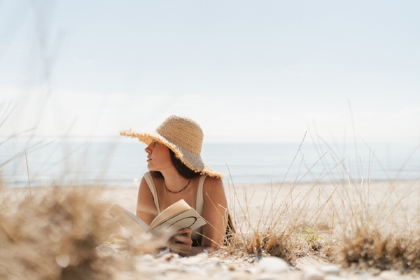 Photo of a young woman enjoying a day at the beach and reading a book