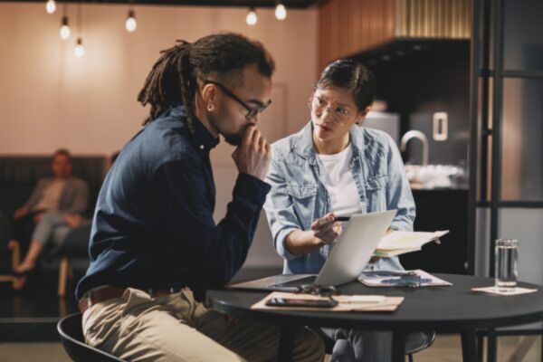 Two colleagues working together to solve a problem, looking at laptop and files.