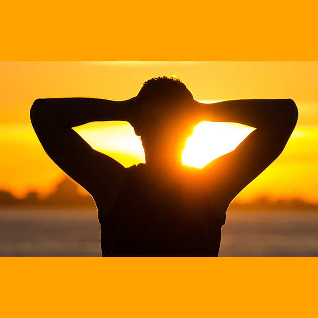 Silhouette of person with hands behind head facing a sunrise